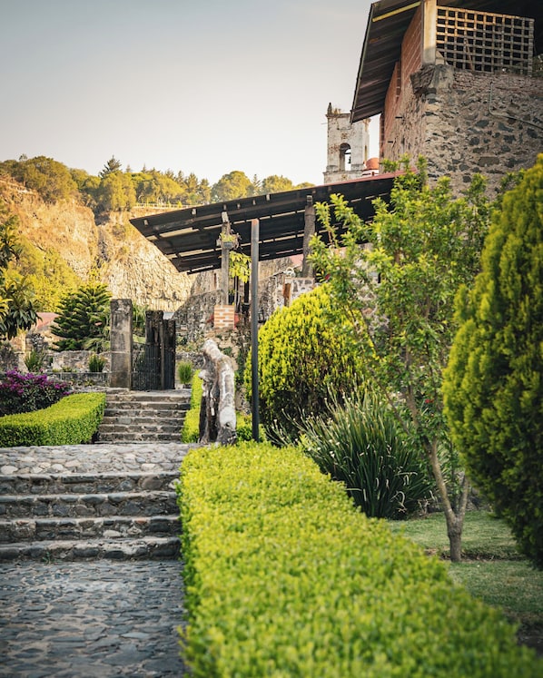 A stone staircase leading to a building with a thatched roof, surrounded by well-maintained hedges and plants. - Hacienda Santa Maria Regla (San Miguel Regla)