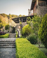 Una escalera de piedra conduce a un edificio con techo de paja, rodeado de setos y plantas bien cuidados.