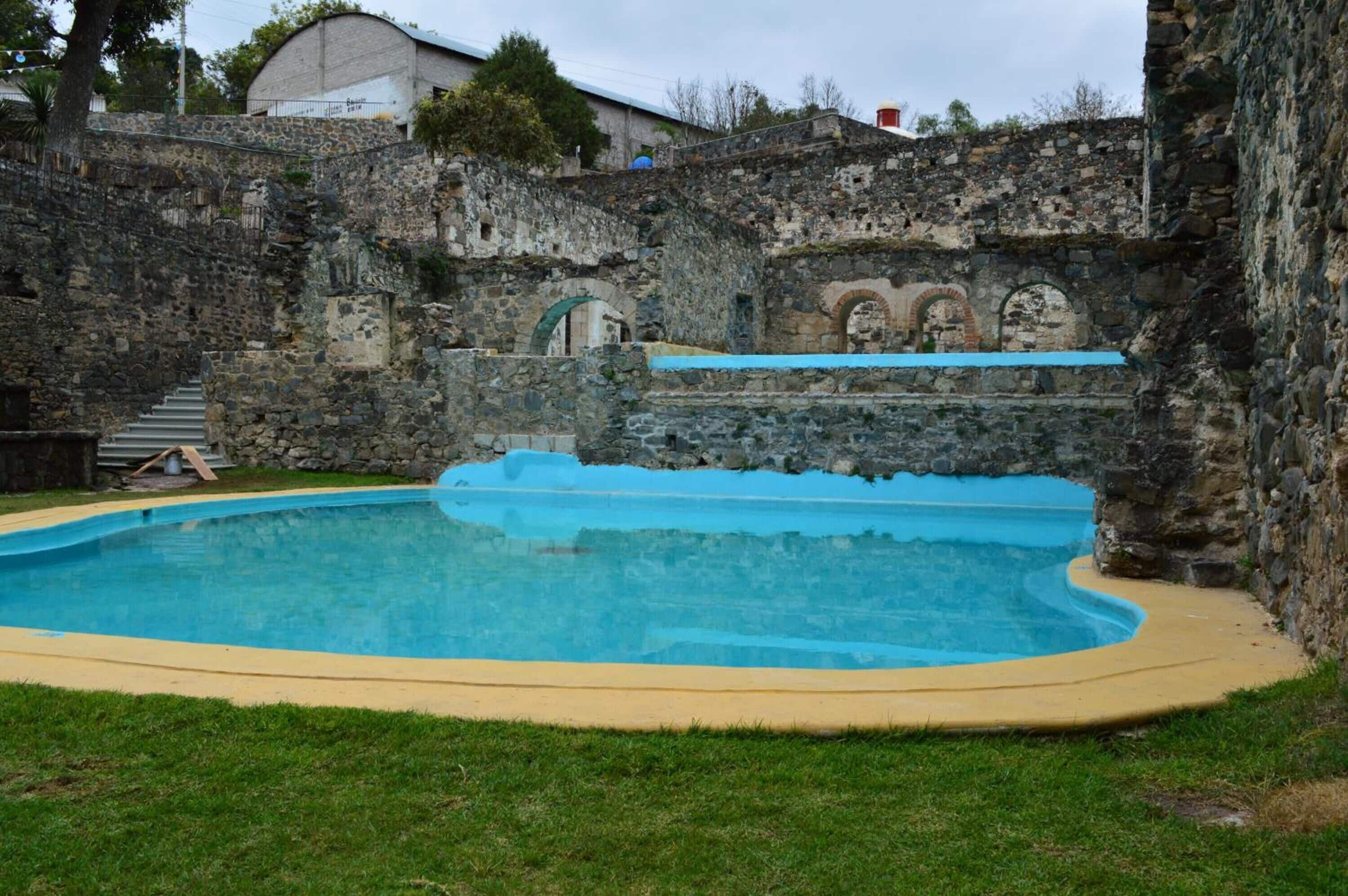 A swimming pool with stone walls and a grassy area.