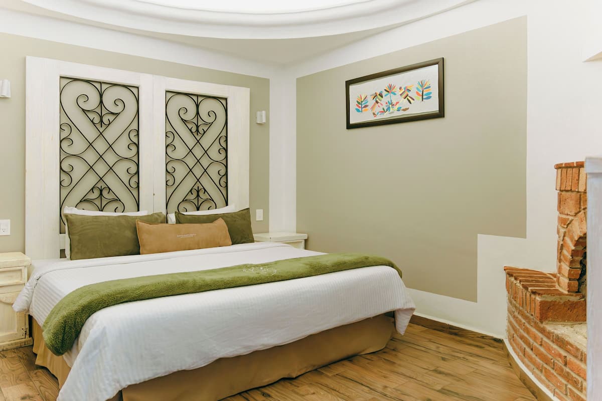 A bedroom with a bed, a green throw, a brick fireplace, and a decorative wall panel.