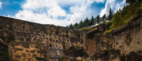 Una antigua estructura de piedra con una escalera que lleva a una entrada en arco, rodeada por un pequeño estanque y un sendero de piedra.