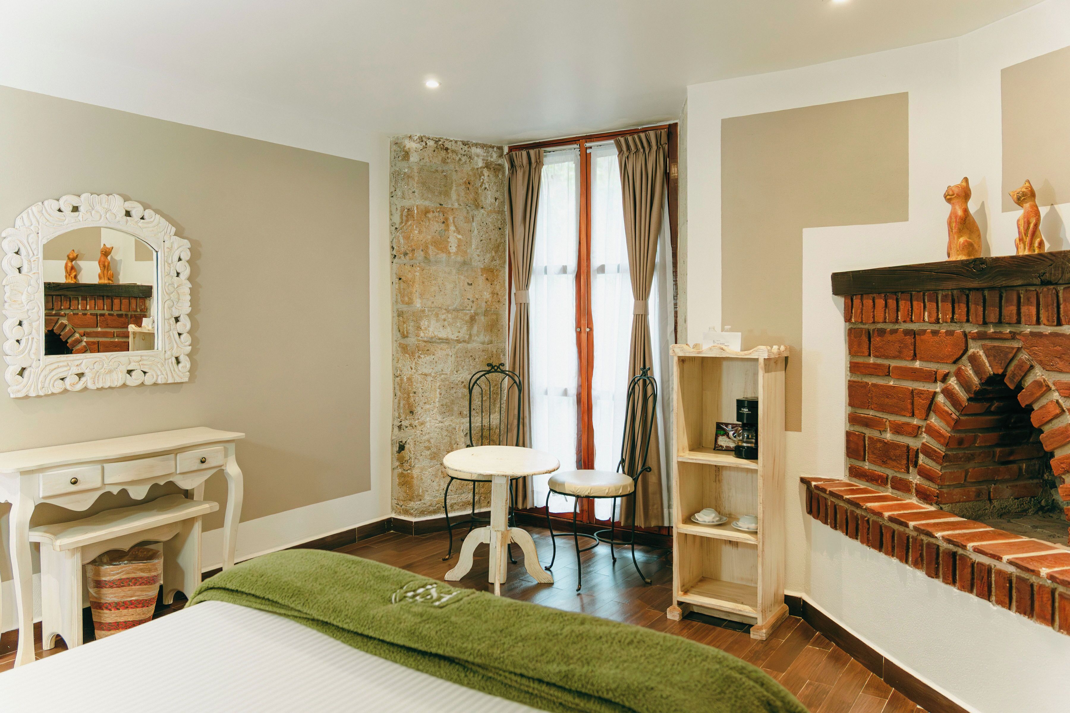 A bedroom with a bed, a desk, a chair, a fireplace, and a mirror.