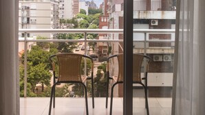 A balcony with a view of the city, a bed, and two wicker chairs. - 27 Suites Apart Hotel (Montevideo)
