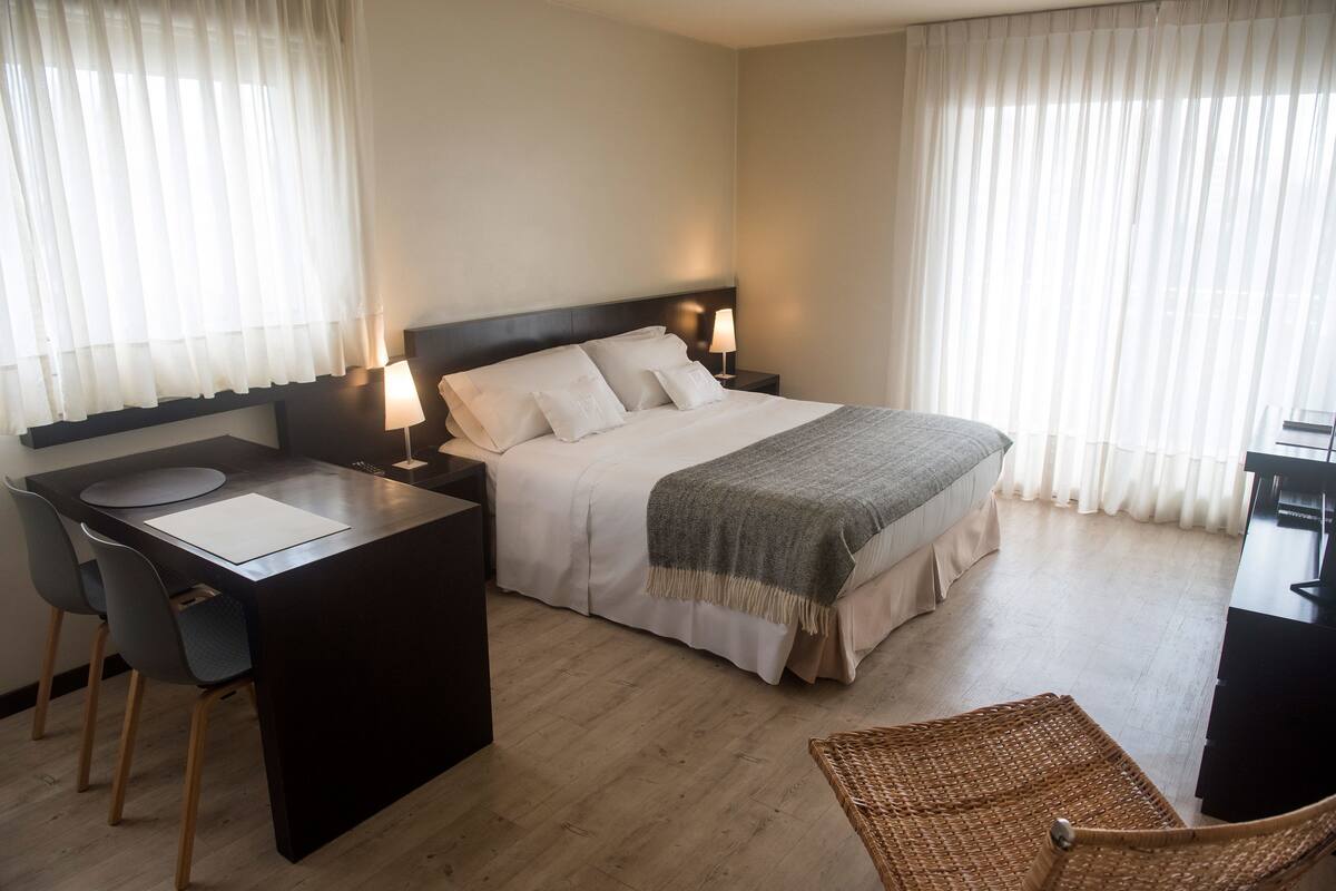 A hotel room with a bed, desk, chair, and curtains.