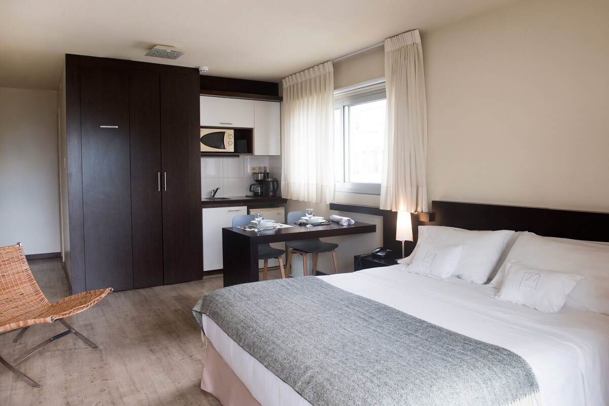 A hotel room with a bed, a desk with a chair, a wardrobe, and a window with curtains.