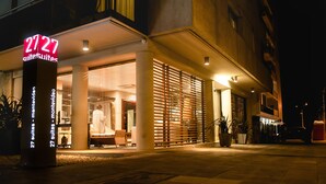 A hotel entrance with a neon sign, large columns, and a covered outdoor seating area. - 27 Suites Apart Hotel (Montevideo)