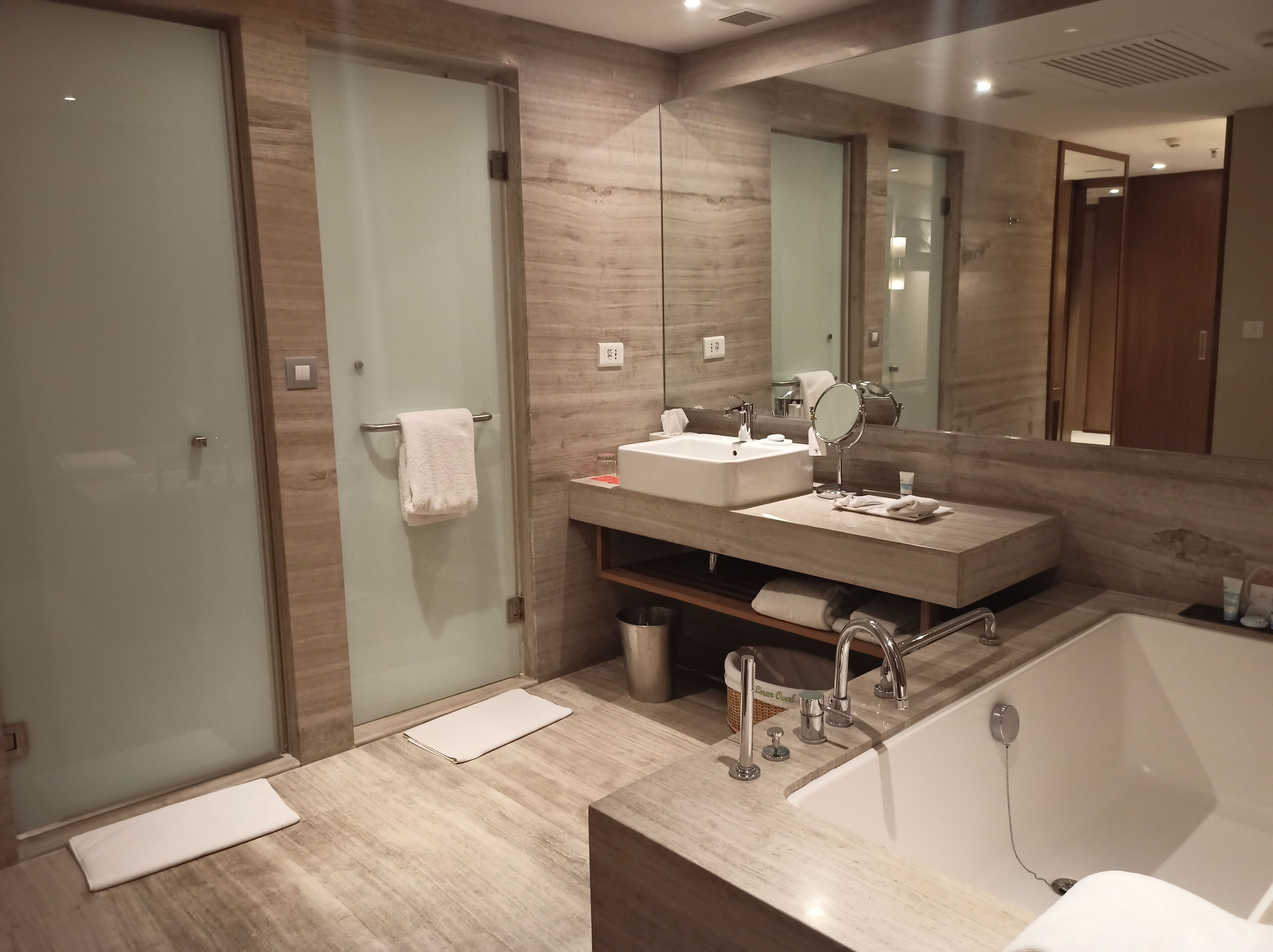 Une salle de bain moderne avec une douche à l’italienne en verre, un grand lavabo avec un miroir et une baignoire séparée.