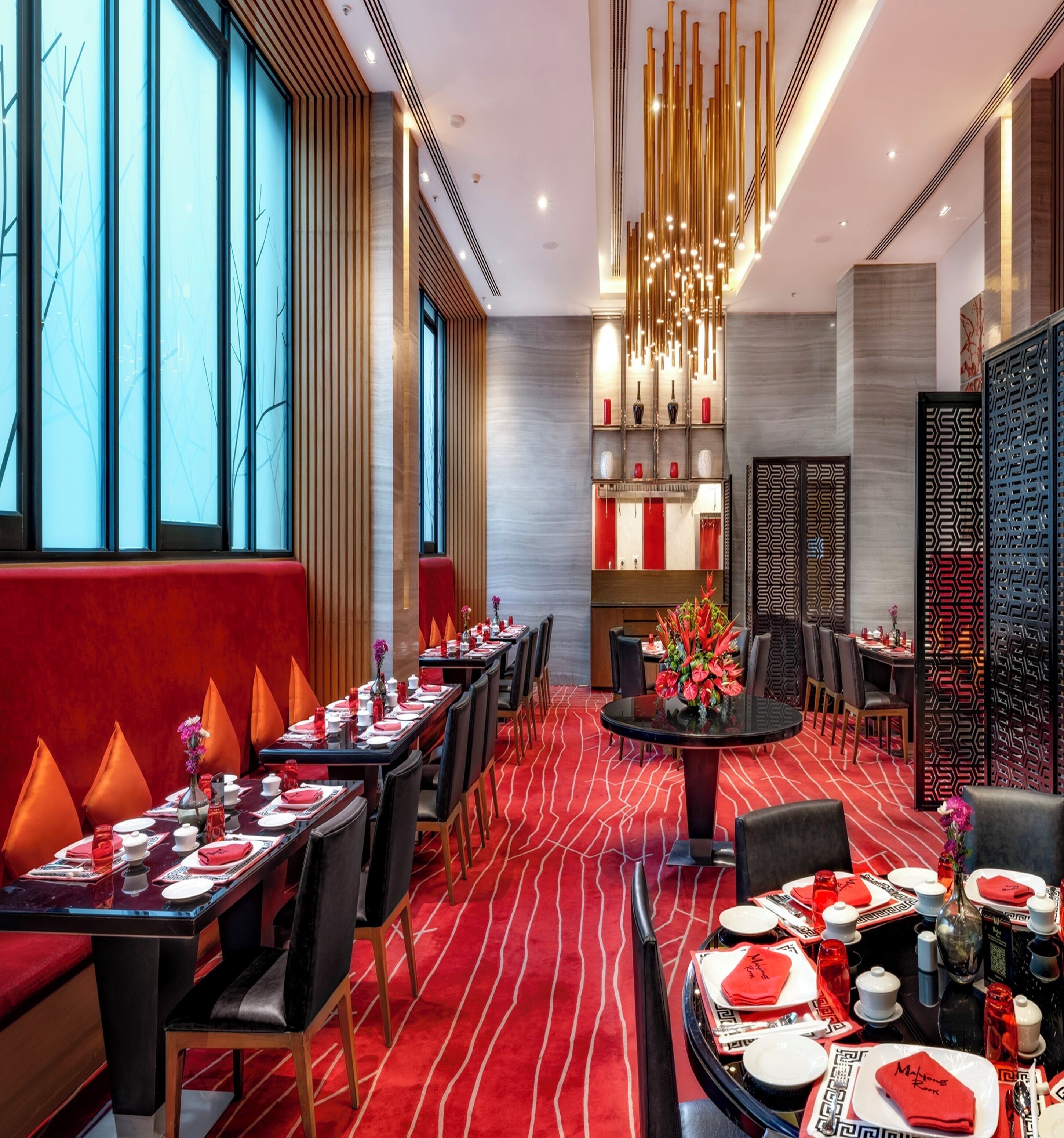 A modern restaurant with red and black decor, featuring long tables, chairs, and a central decorative piece.