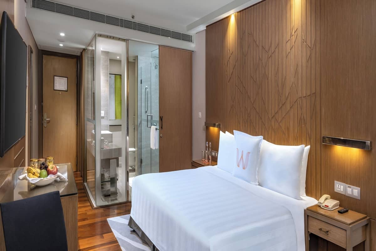 A modern hotel room with a large bed, a desk with a telephone, and a glass shower enclosure.
