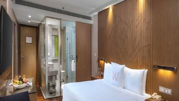 A modern hotel room with a large bed, a desk with a telephone, and a glass shower enclosure.