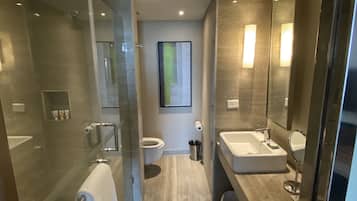 Un bany modern amb una dutxa envidriada, un mirall gran, un vàter i un lavabo amb calaixera.
