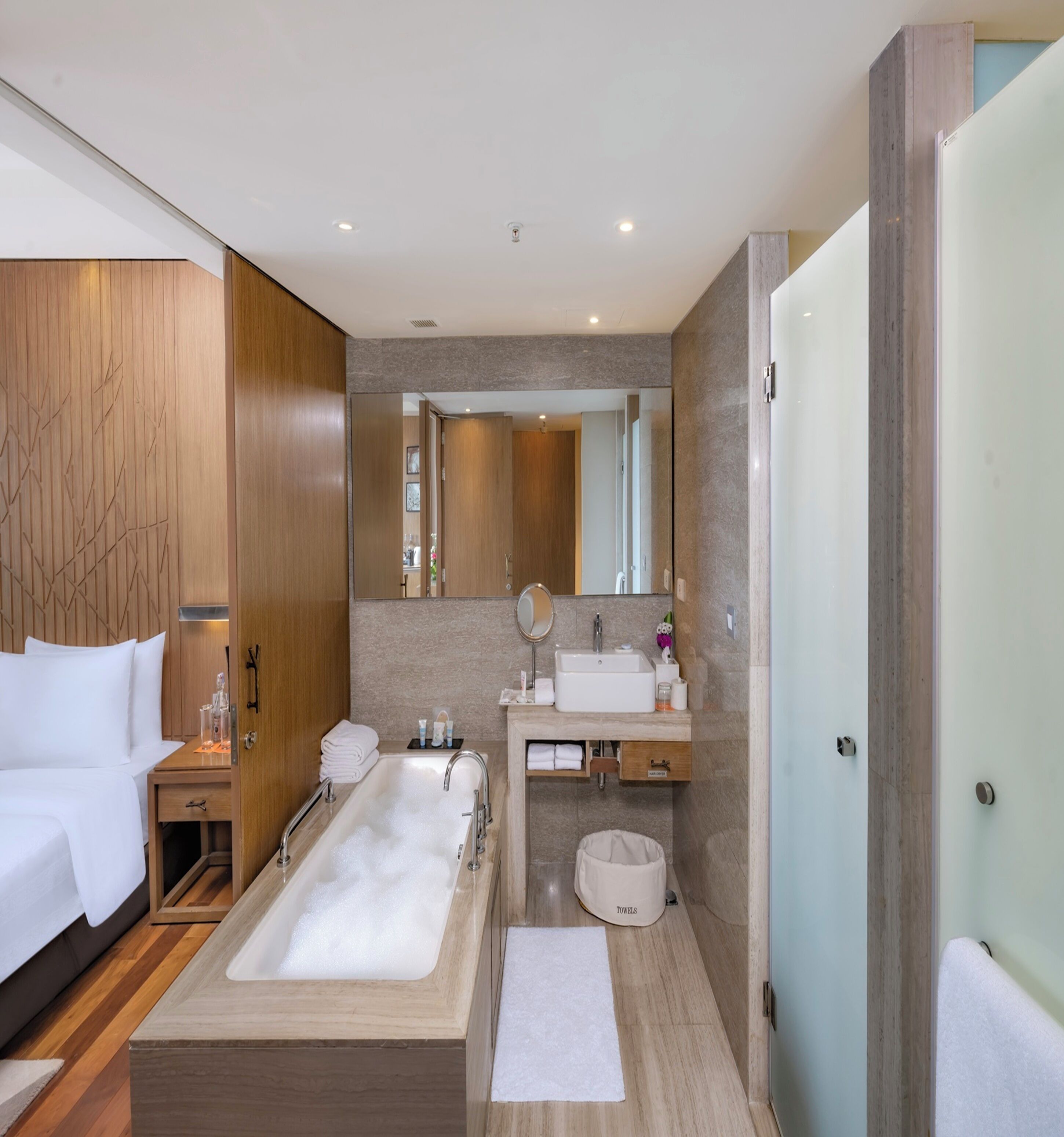 A modern hotel bathroom with a large bathtub, a separate shower area, a vanity with a mirror, and a toilet.