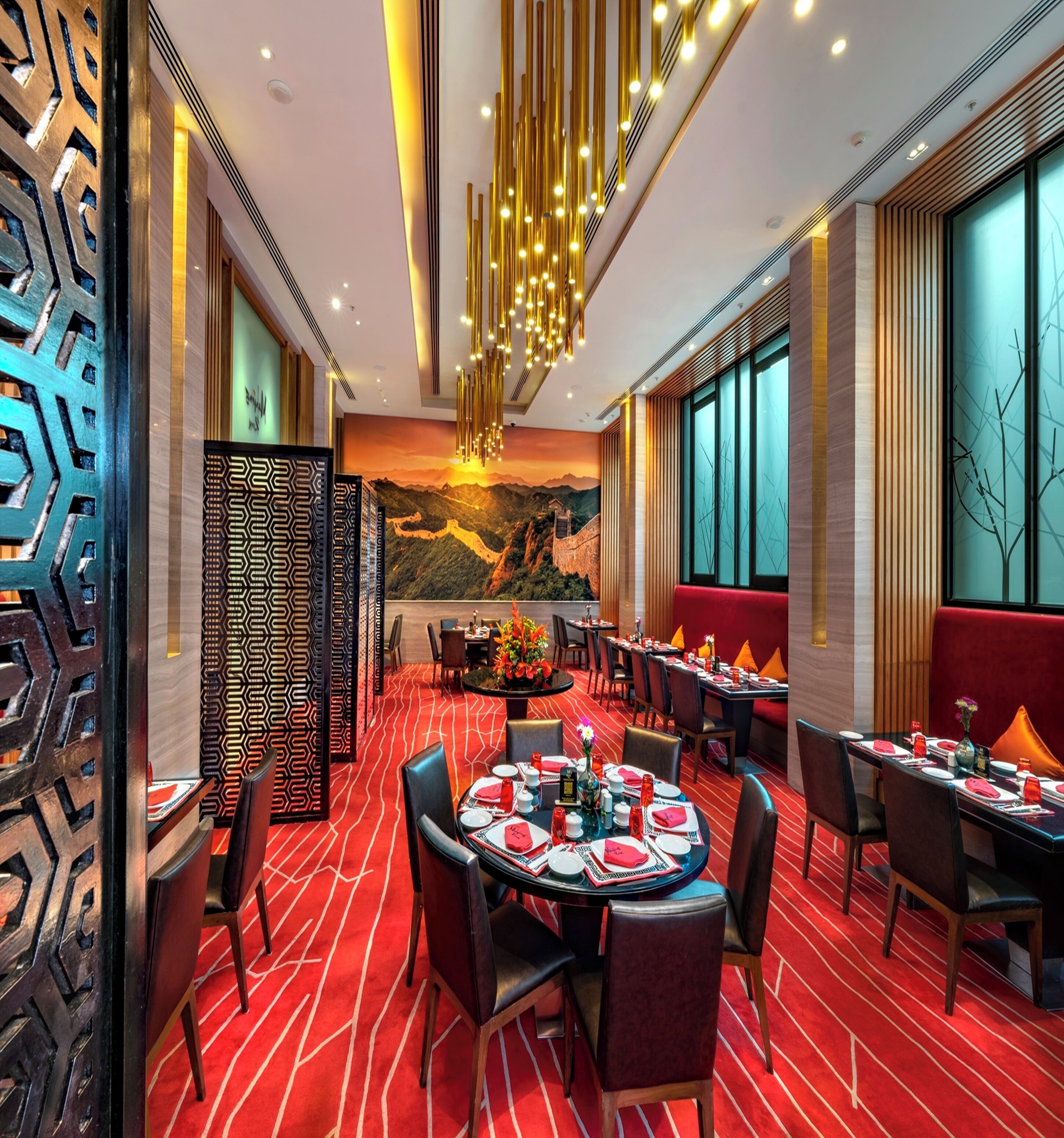 Ein Restaurant mit runden Tischen, rotem Teppichboden und einem Wandbild der Chinesischen Mauer.