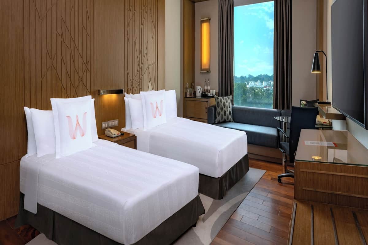 A hotel room with two beds, a desk, a chair, a TV, and a window with a view.
