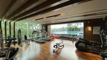 A spacious gym with treadmills, ellipticals, and free weights. Large windows offer views of greenery and a pool.