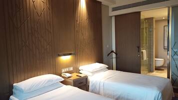 Quarto de hotel com duas camas, uma mesa de cabeceira com telefone e uma luminária na parede.