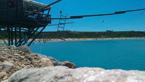 A coastal scene with a rocky foreground, a beach, and a pier with a structure on it. - B&B Le Pietre Ricce (Roccamontepiano)