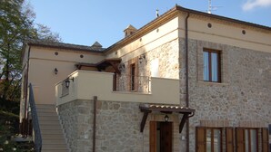 A two-story stone building with a balcony, a staircase, and a door.