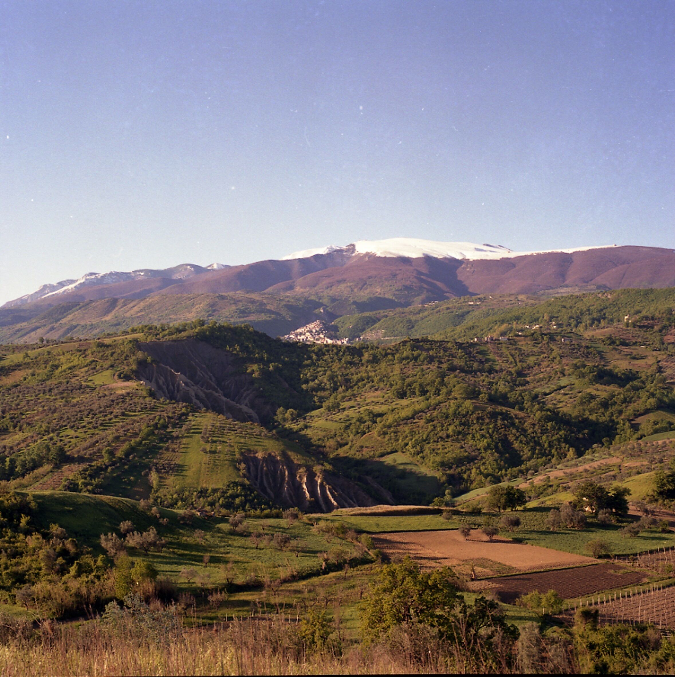 Eine gebirgige Landschaft mit einem Tal, Feldern und einer kleinen Siedlung.