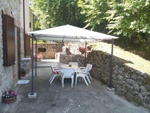 An outdoor patio with a table and chairs under a white canopy, surrounded by stone walls and greenery. - B&B Le Pietre Ricce (Roccamontepiano)