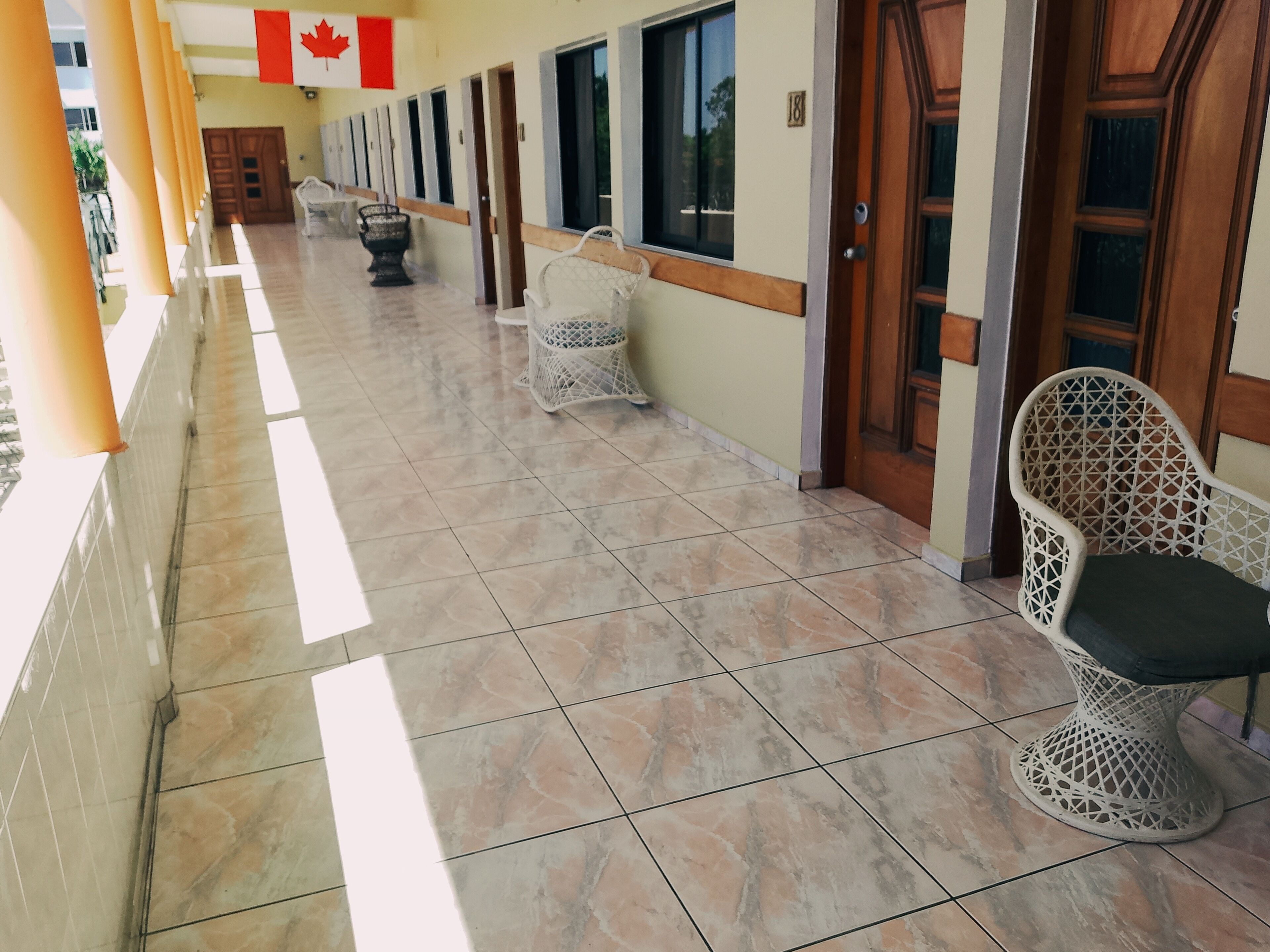 A corridor with tiled flooring, white wicker chairs, and doors numbered 18.