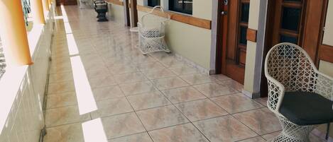 A corridor with tiled flooring, white wicker chairs, and doors numbered 18.