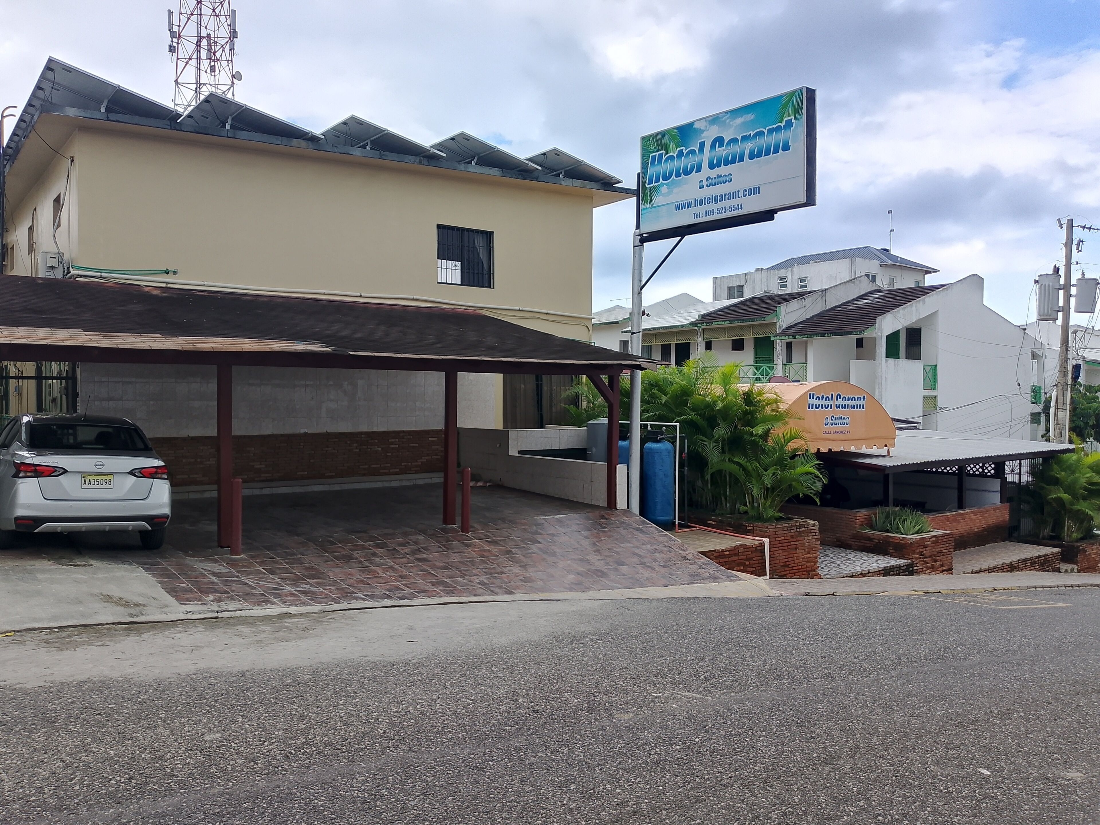 Um edifício com uma placa indicando 'Hotel Garant & Suites' e uma área de estacionamento coberta, onde se vê um carro branco.
