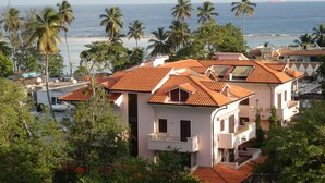 Uma área residencial costeira com casas de telhado de terracota, palmeiras e vista para o mar.