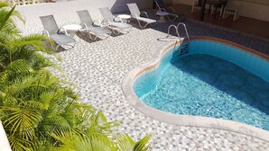 Piscina com espreguiçadeiras e deck revestido de azulejos.