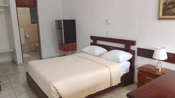 Ein Hotelzimmer mit Bett, Nachttisch mit Lampe, Fernseher und einer Tür zu einem Badezimmer.
