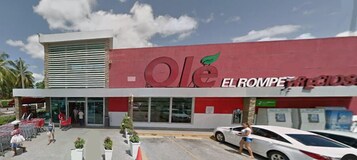 Uma loja chamada 'ole' com fachada vermelha e branca, grandes janelas e um estacionamento com carros e carrinhos de compras.