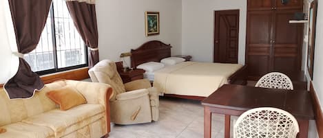 A hotel room with a bed, a sofa, a dining table, and a chair.