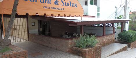 A hotel named 'Hotel Garant & Suites' with a large orange awning, a covered outdoor seating area, and a brick facade.