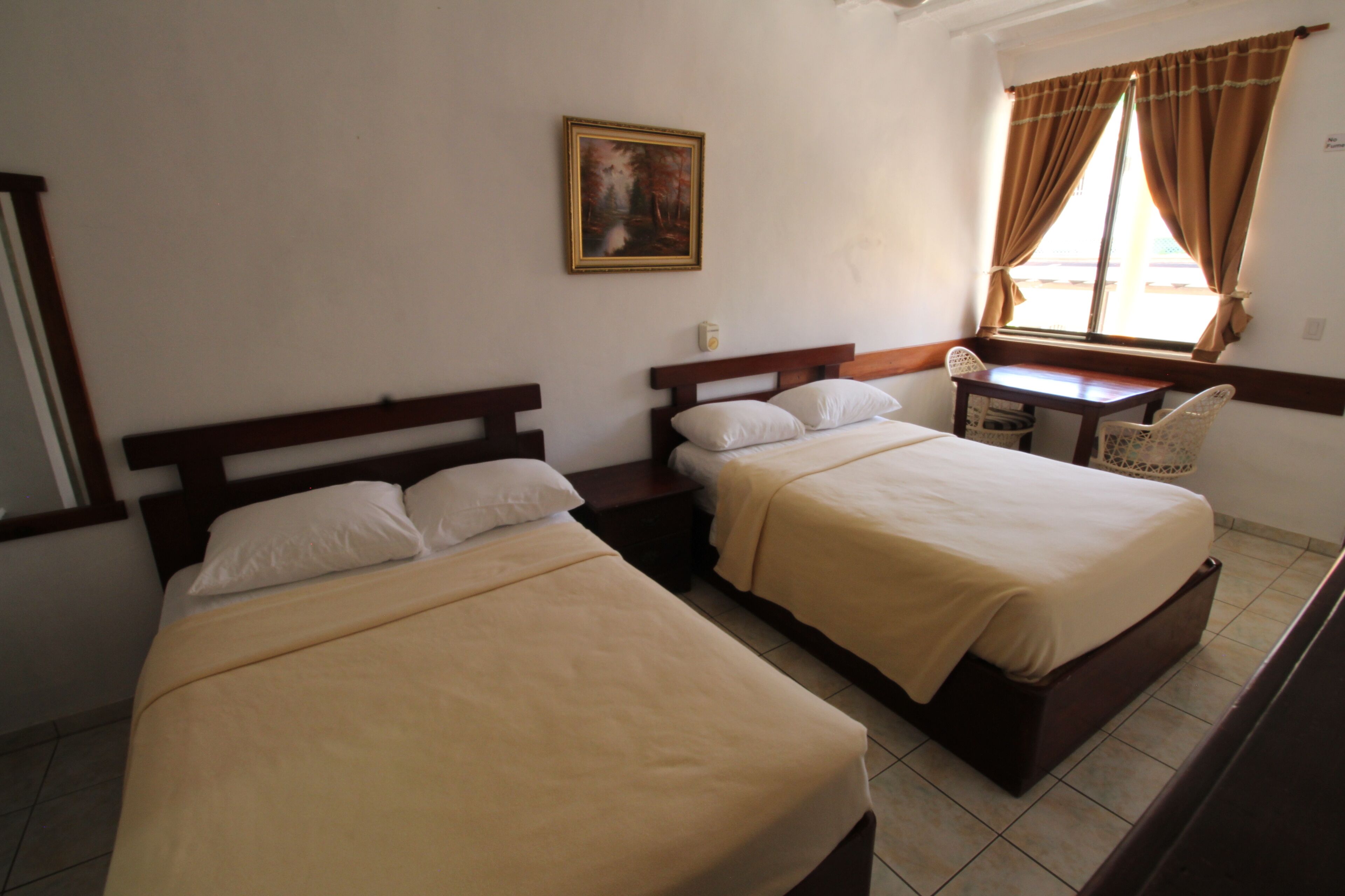 A room with two single beds, a small table, a chair, and a window with curtains.