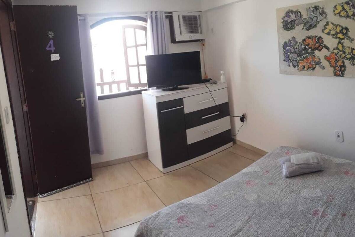 Ein Schlafzimmer mit Bett, Kommode, Fernseher und Fenster.