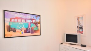 Una habitación con un cuadro grande de una furgoneta antigua, un televisor sobre un mueble y un cuadro más pequeño de la Torre Eiffel.