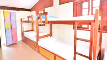 Three cozy beds line the room, each with a mattress and wooden frame, set against a colorful wall art and a window with wooden shutters.