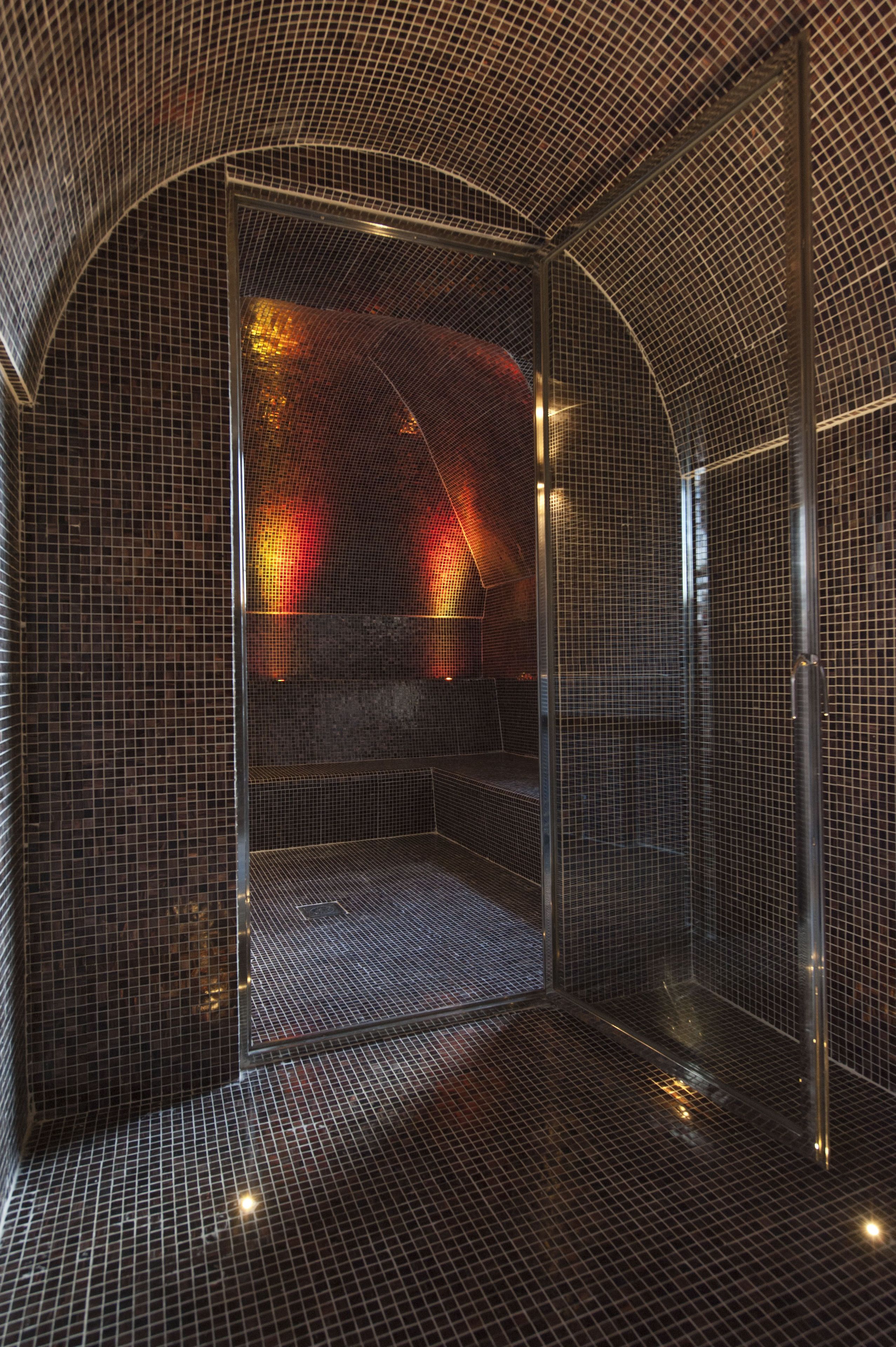 A modern, enclosed shower area with a curved, metallic mesh ceiling and walls, featuring a textured floor and a visible bench.