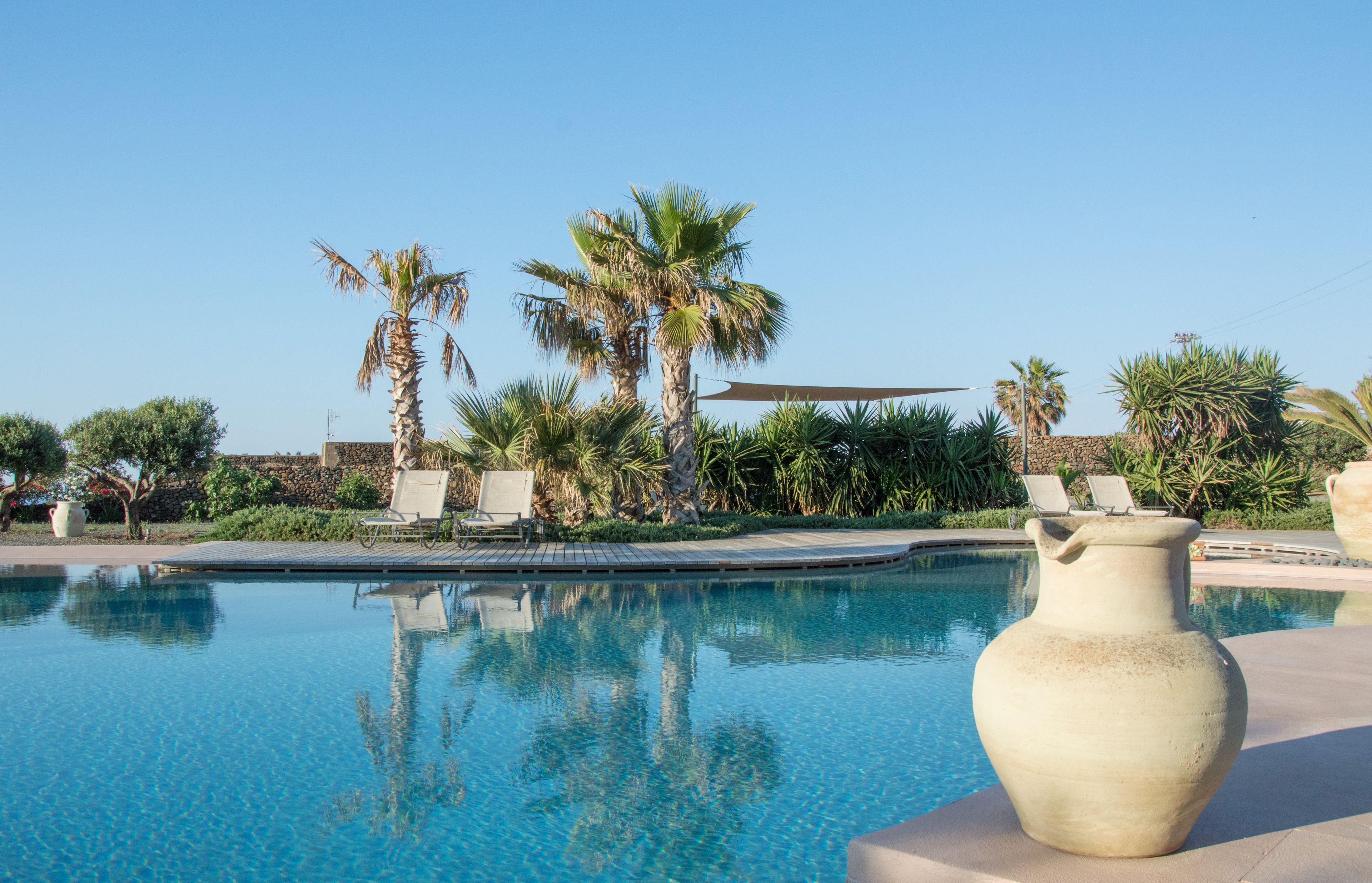 A clear swimming pool with lounge chairs and palm trees.