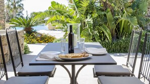 An outdoor dining area with a table and chairs, surrounded by lush tropical plants and a view of the ocean. - Resort Acropoli (Pantelleria)