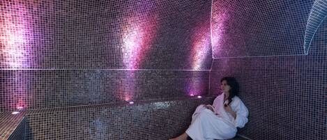 Una persona sentada en una habitación con paredes de azulejos, techo curvo e iluminación rosada.