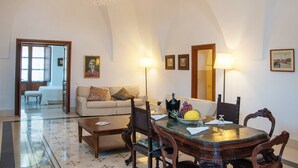 A spacious living room with a high arched ceiling, a chandelier, a dining table with chairs, a sofa, and a coffee table. - Resort Acropoli (Pantelleria)