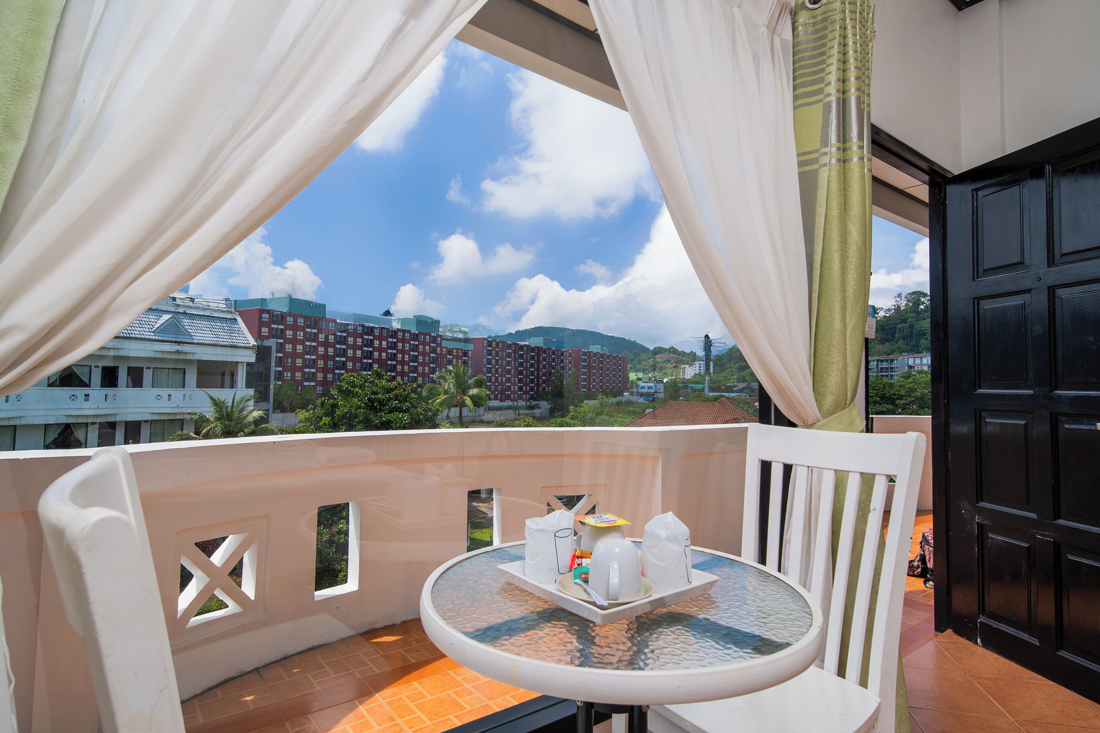 A balcony with a table set for two, a chair, and a view of buildings and hills.