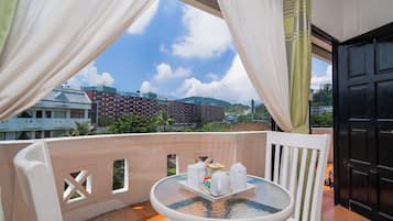 A balcony with a table set for two, a chair, and a view of buildings and hills.