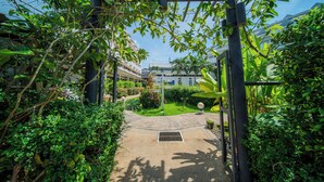 A pathway leading to a building with a traditional architectural style, surrounded by lush greenery and a clear blue sky. - Blue Carina Hotel (Wichit)