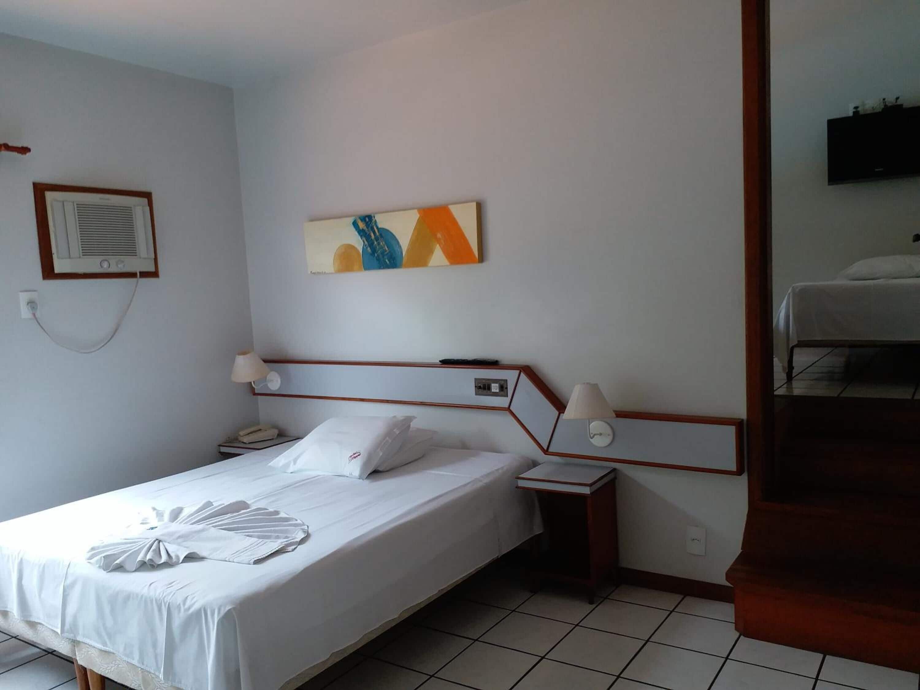 Una habitación de hotel con cama, mesita de noche, lámpara y un cuadro en la pared.