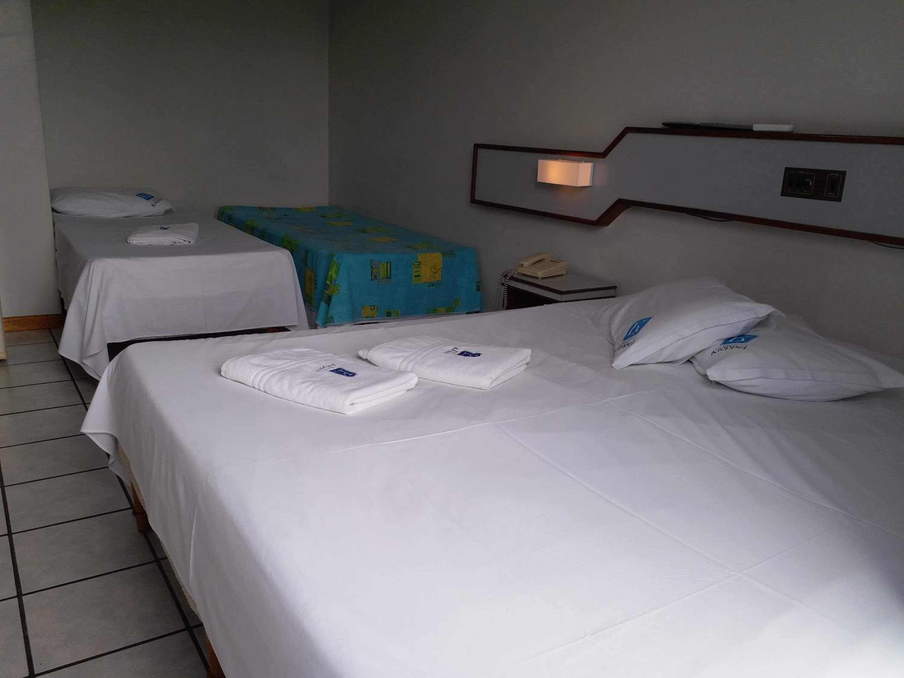 Habitación de hotel con dos camas, cada una con toallas y almohadas bien ordenadas.