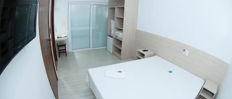Un dormitorio moderno con cama, estanterías empotradas, escritorio y un armario con puerta corredera de vidrio.