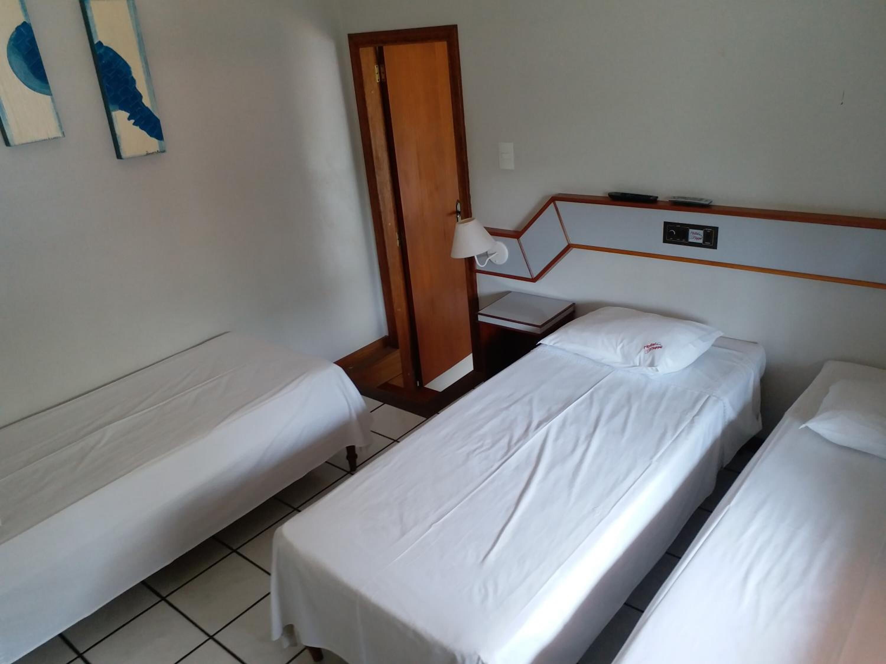 A hotel room with two single beds, a wooden door, a small table with a lamp, and a wall-mounted TV.