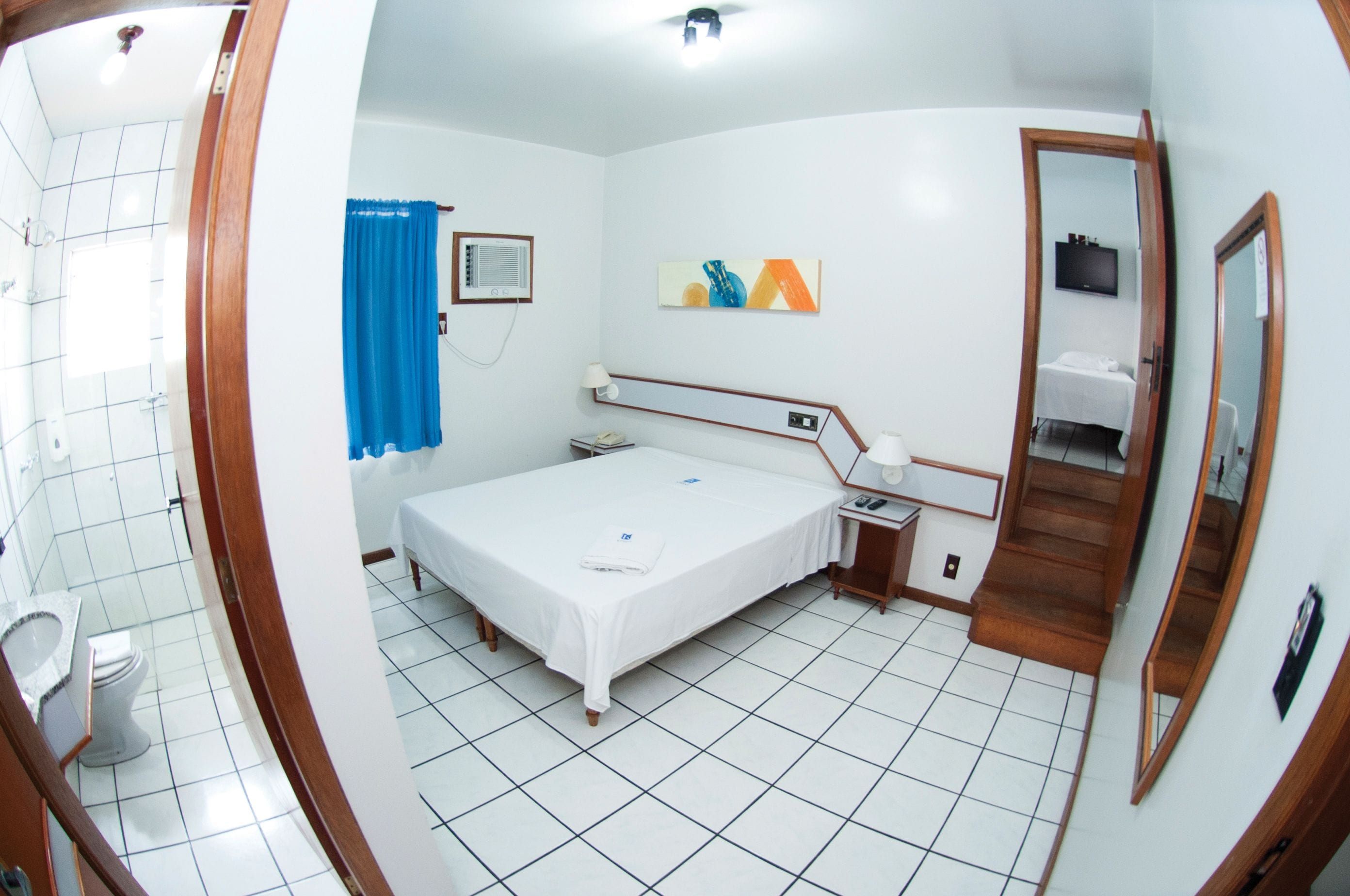 Habitación de hotel con cama, escritorio, silla, espejo, ventana con cortinas, inodoro y zona de ducha.